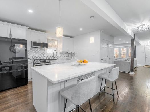 A kitchen with white cabinets , a large island , and stools.