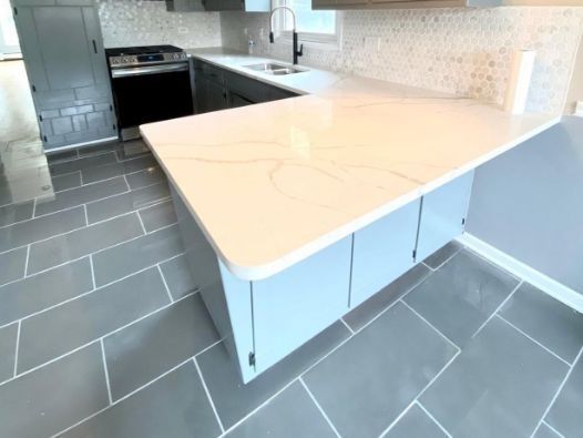 A kitchen with a white counter top and gray tile floor.