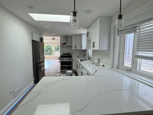 A kitchen with white cabinets , a stove , a refrigerator , and a window.