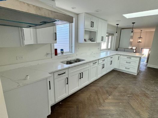 A kitchen with white cabinets , a sink , and a window.