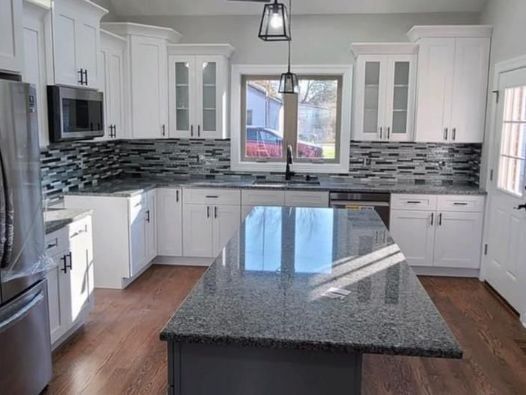 A kitchen with white cabinets , granite counter tops , stainless steel appliances and a large island.