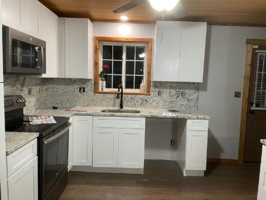 A kitchen with white cabinets , stainless steel appliances , a sink and a window.