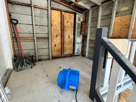 A blue vacuum cleaner is sitting in a room next to a shovel and stairs.