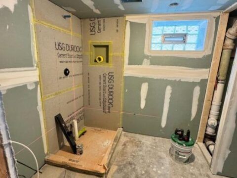 A bathroom under construction with a window and a bucket on the floor.