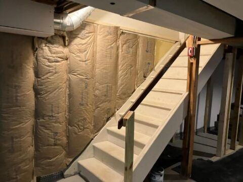 A white staircase in a basement with insulation on the wall.