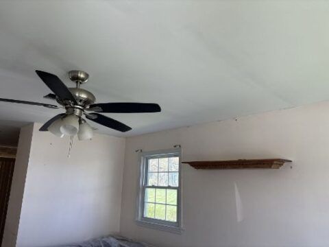 A bedroom with a ceiling fan and a window.