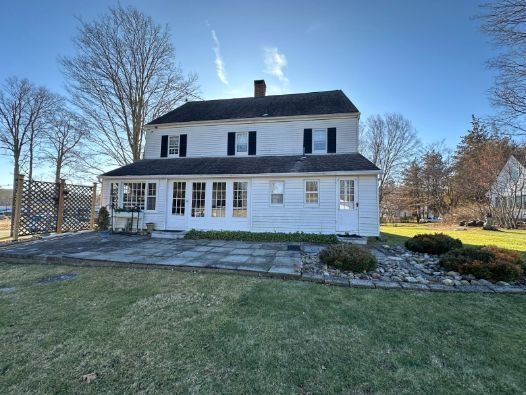 A large white house with black shutters is sitting on top of a lush green field.