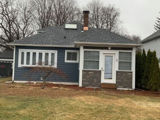 A small blue house with a gray roof and a chimney in the backyard.