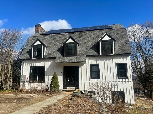 A white house with black windows and solar panels on the roof.