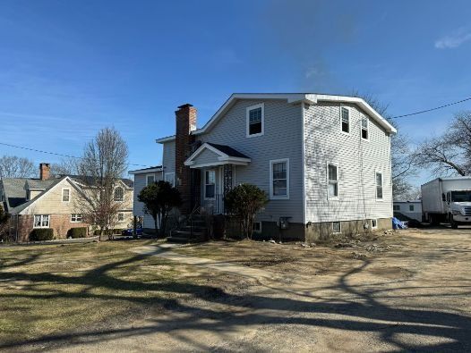 A large white house is sitting in the middle of a dirt field.