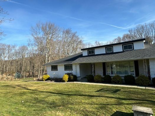A white house with a black roof is sitting on top of a lush green field.
