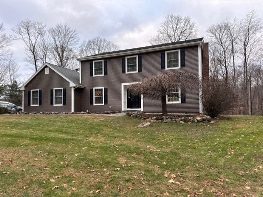 A large brown house with black shutters is sitting in the middle of a grassy field.