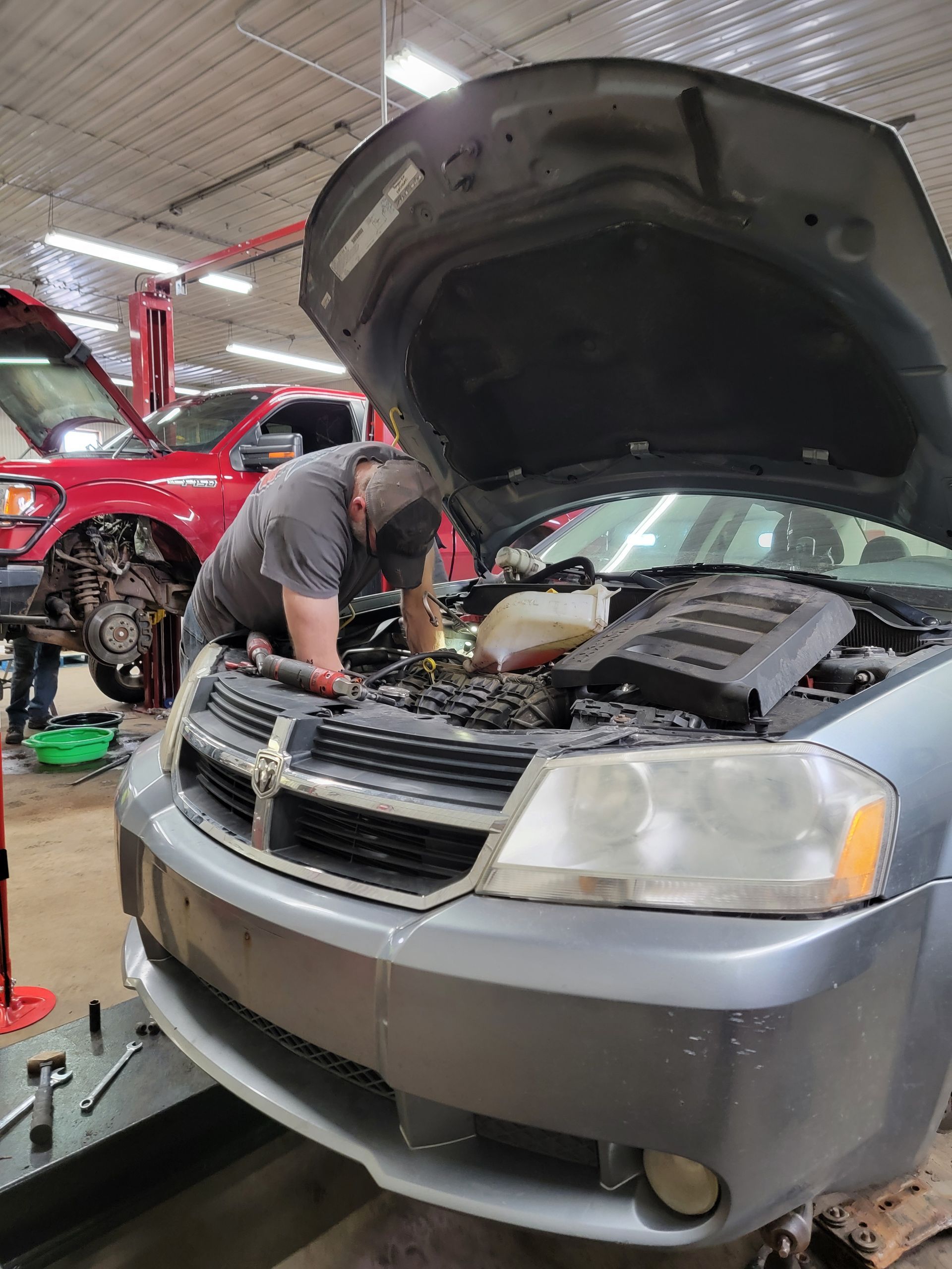 A man is working under the hood of a car in a garage.