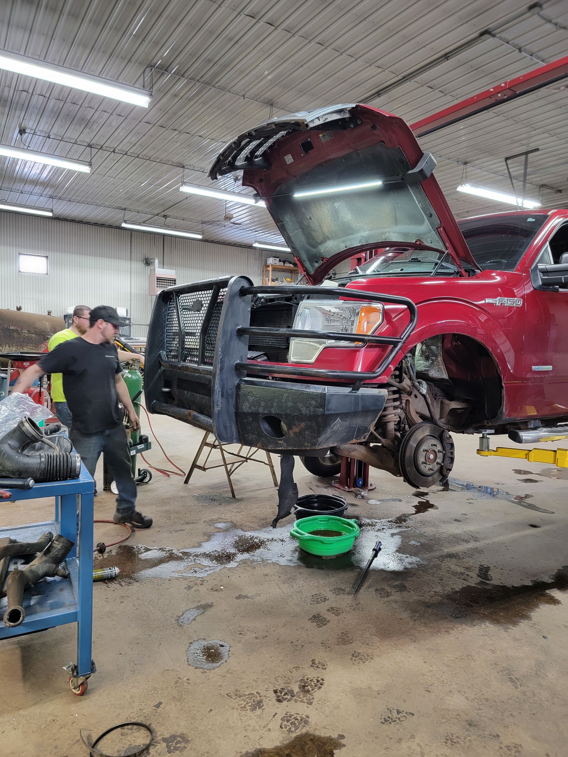 A red truck is being worked on in a garage with the hood open.