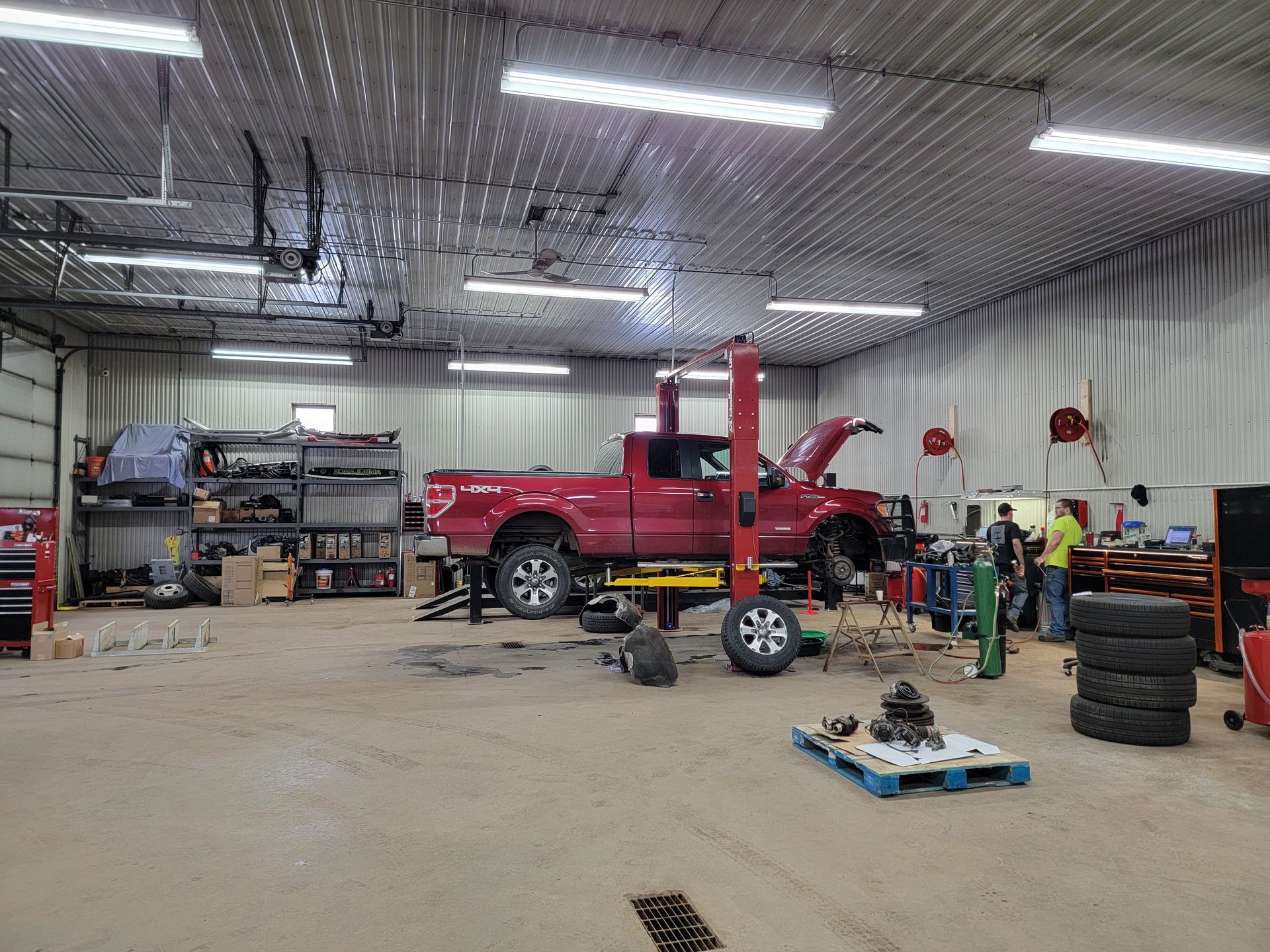 A red truck is being worked on in a garage with the hood open.