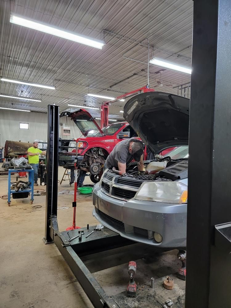 A man is working on a car in a garage with the hood open.