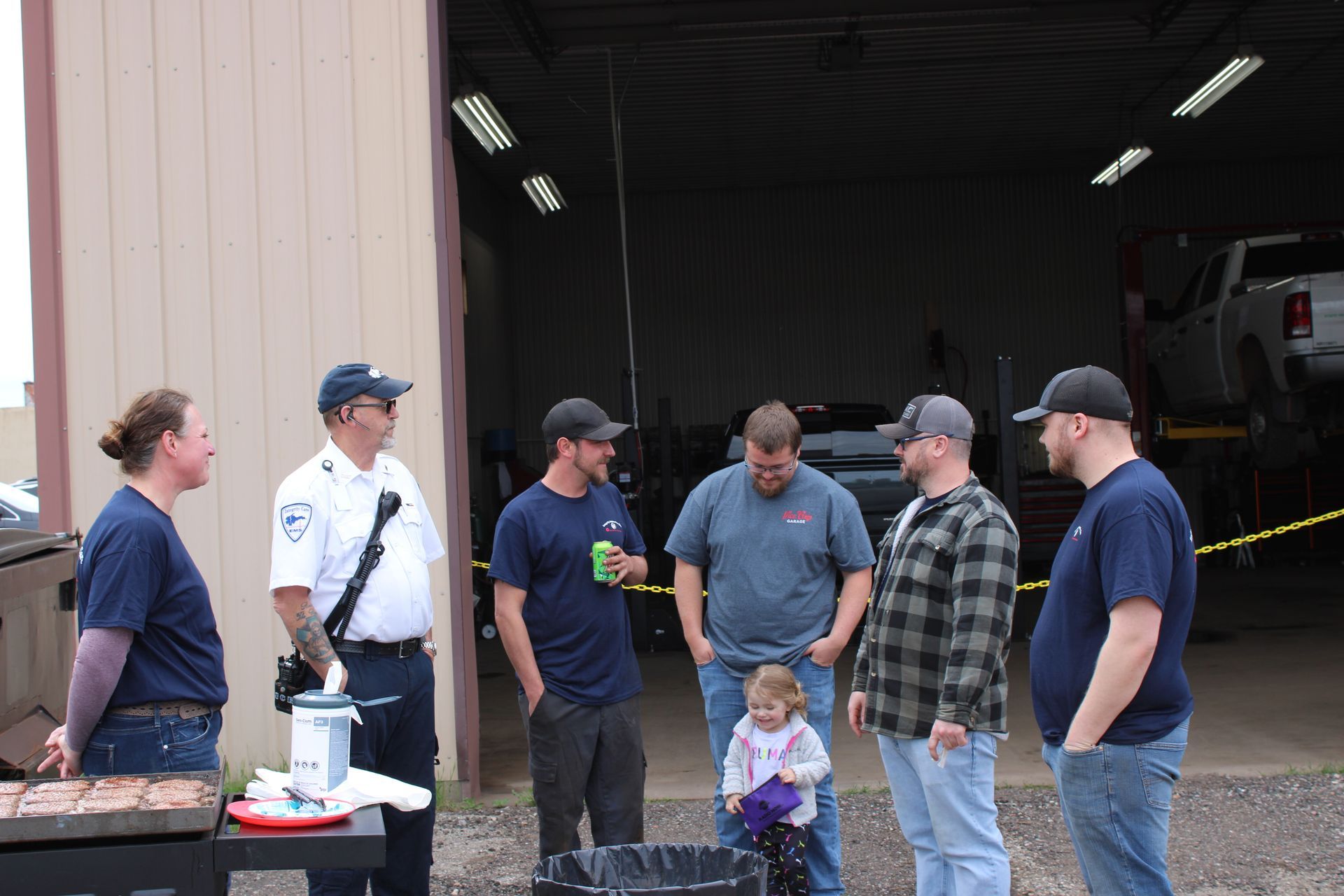 A group of people are standing in front of a garage talking to each other.