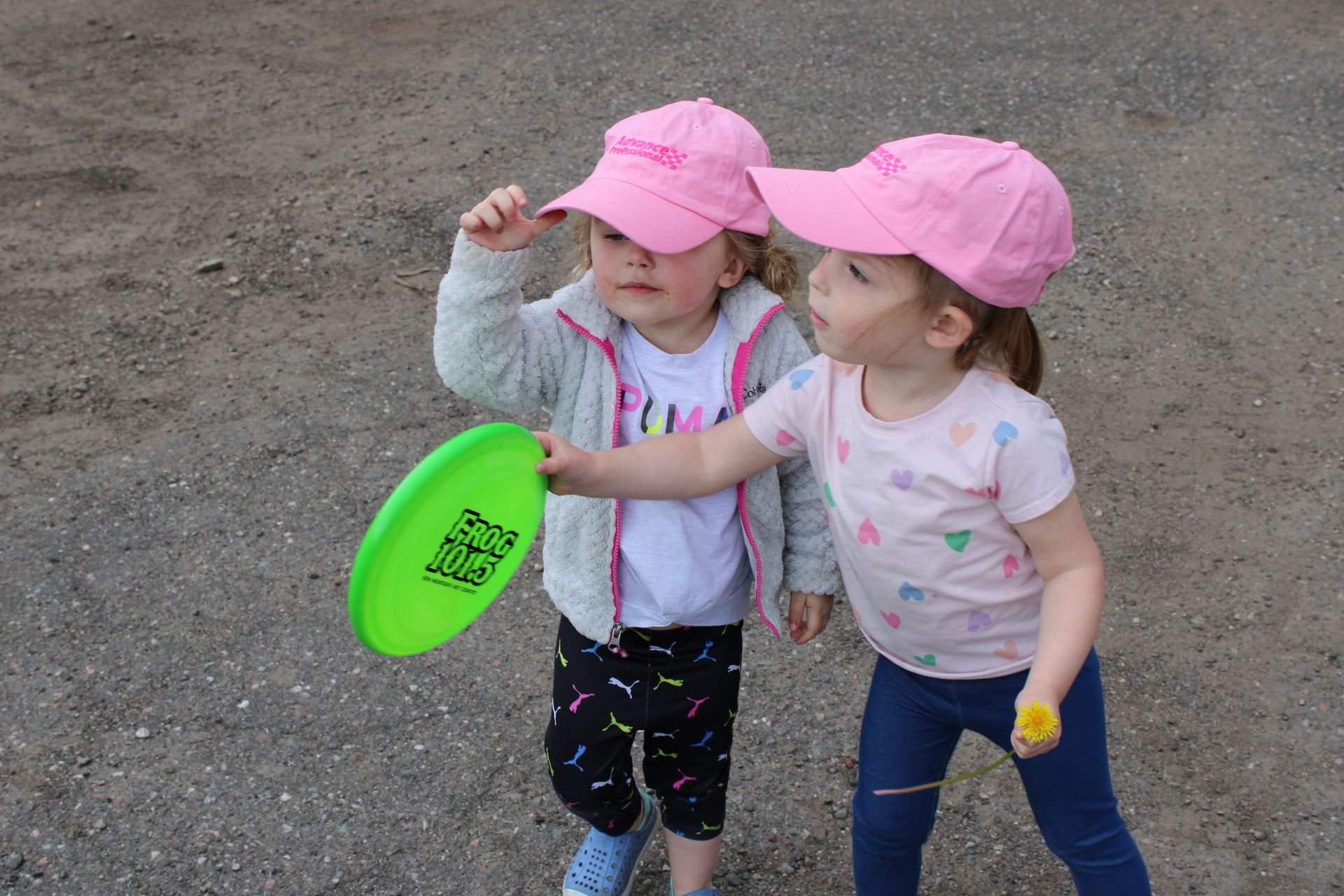 Two little girls wearing pink hats are playing with a frisbee.