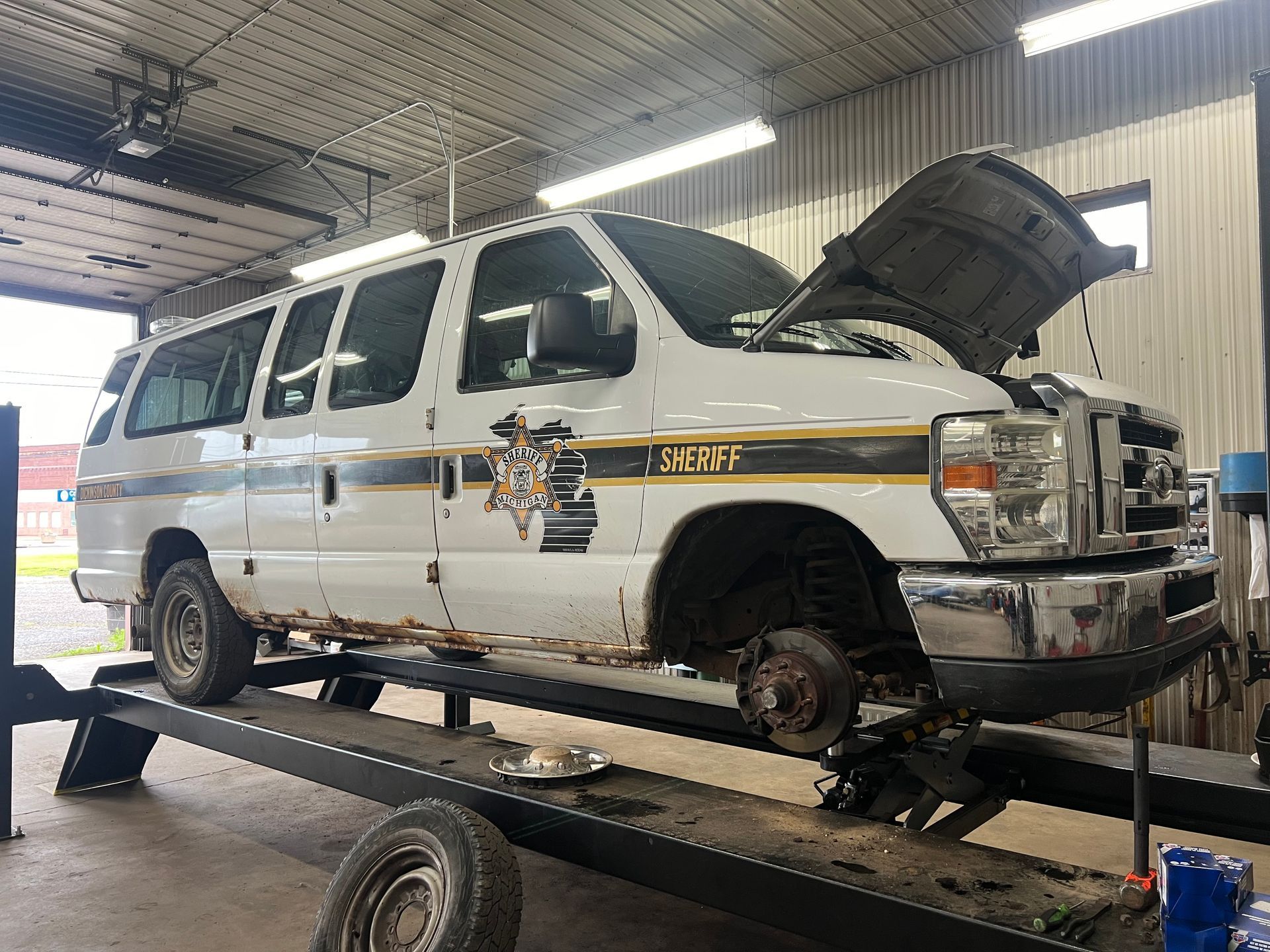 A white van with the hood up is sitting on a lift in a garage.