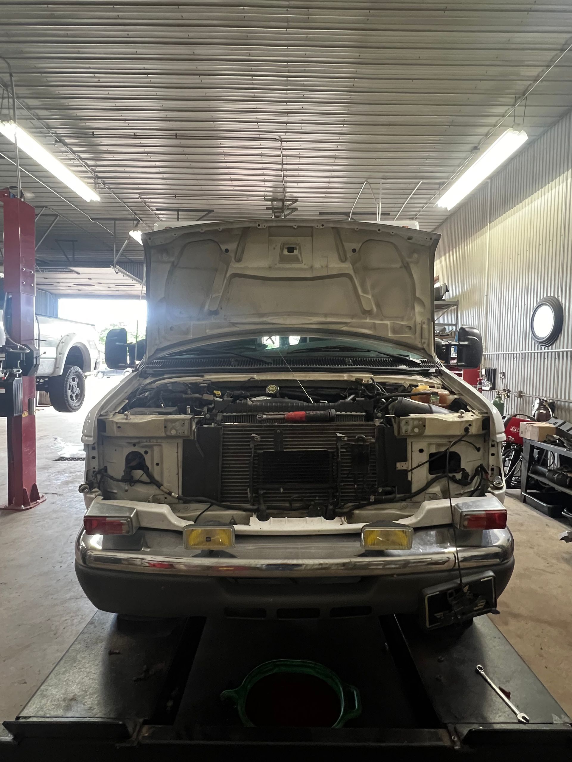 A car with the hood up is sitting on a lift in a garage.