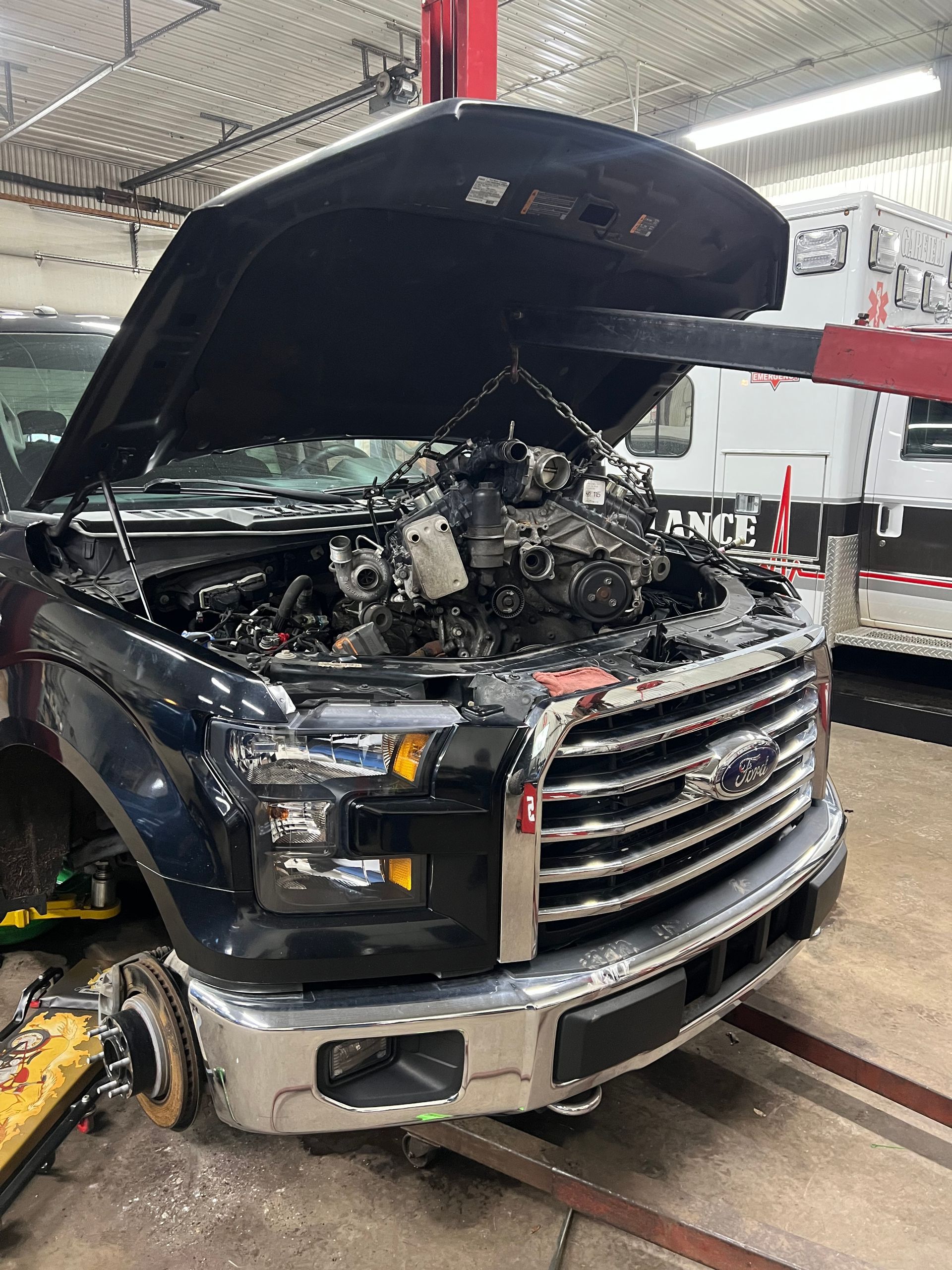 A black ford truck with its hood up in a garage.