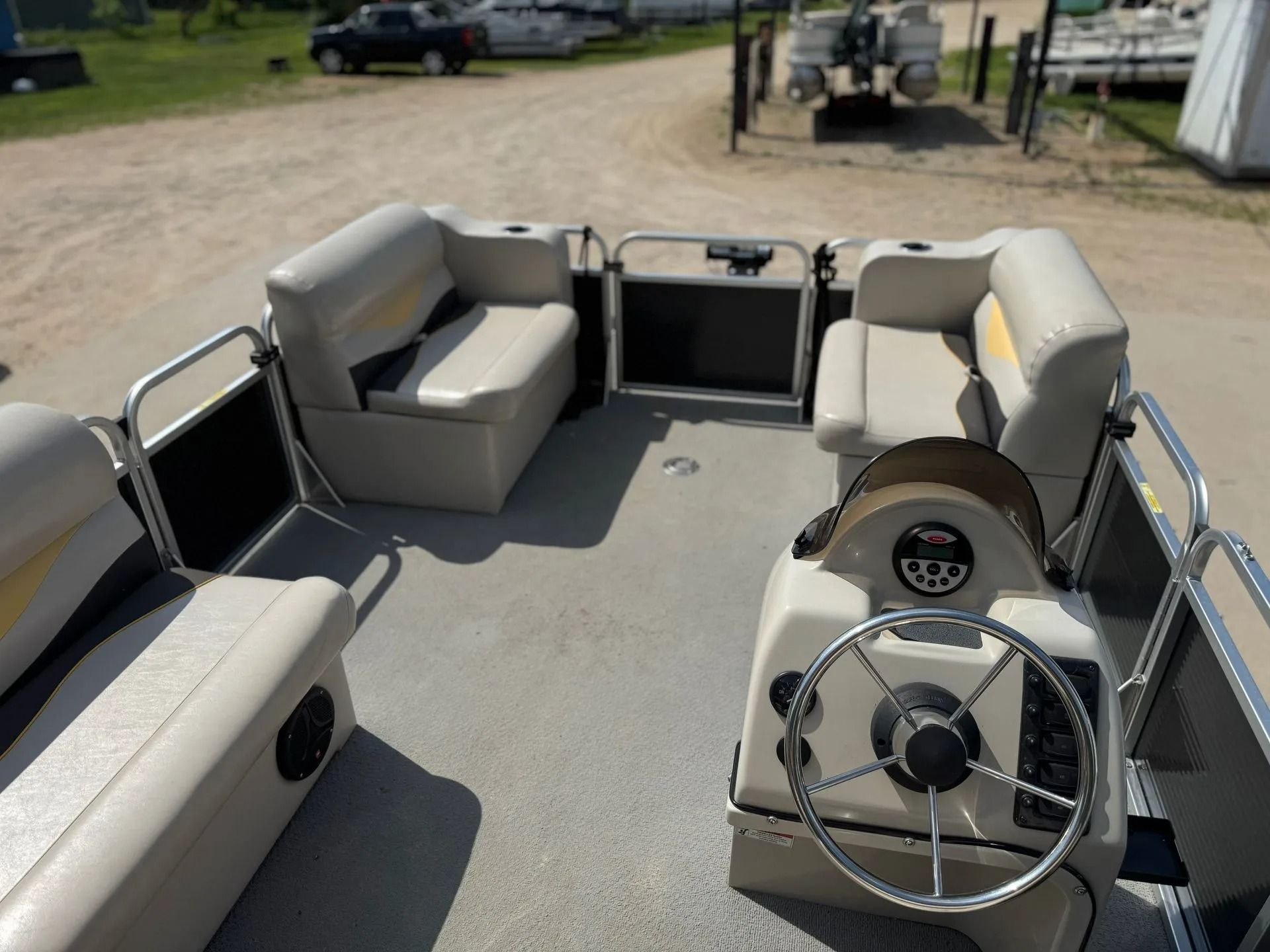 Pontoon boat interior with gray benches and steering wheel, docked outdoors on a sunny day