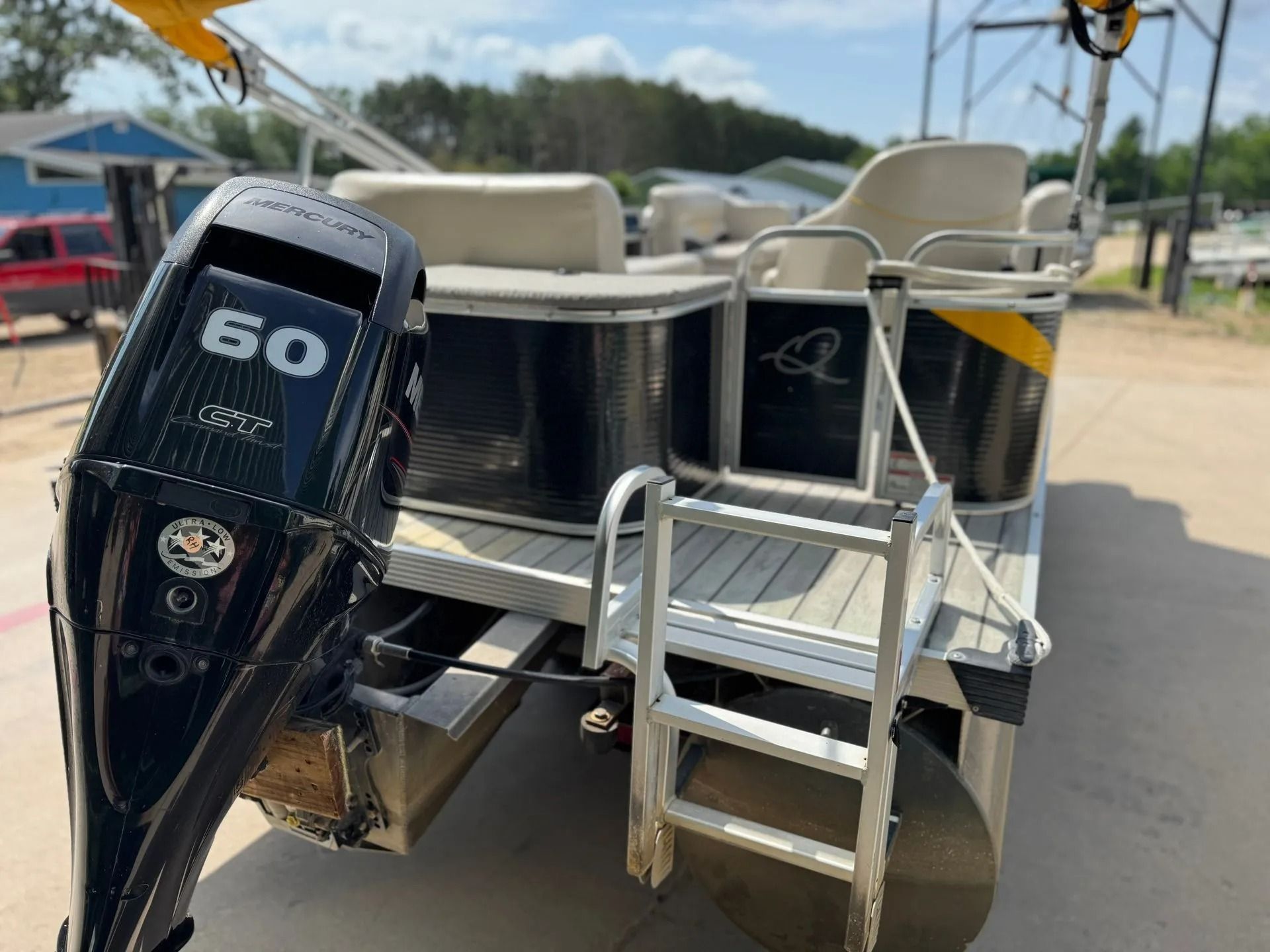 Pontoon boat with 60-hp outboard motor and rear boarding ladder on a paved lot