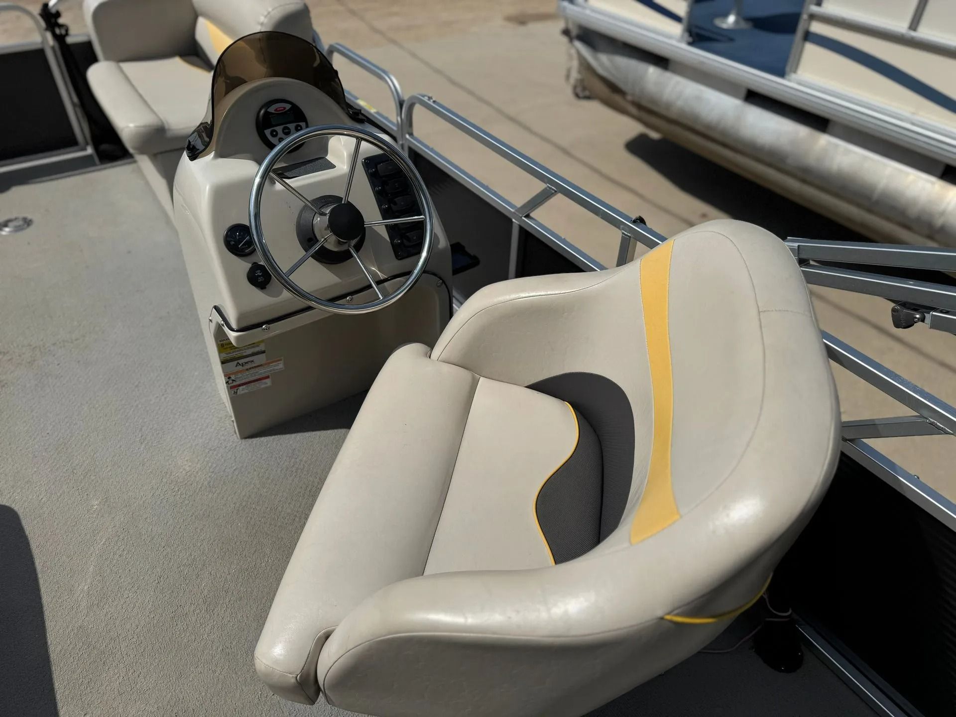 Boat cockpit with gray helm seat, steering wheel, and metal railings on a deck