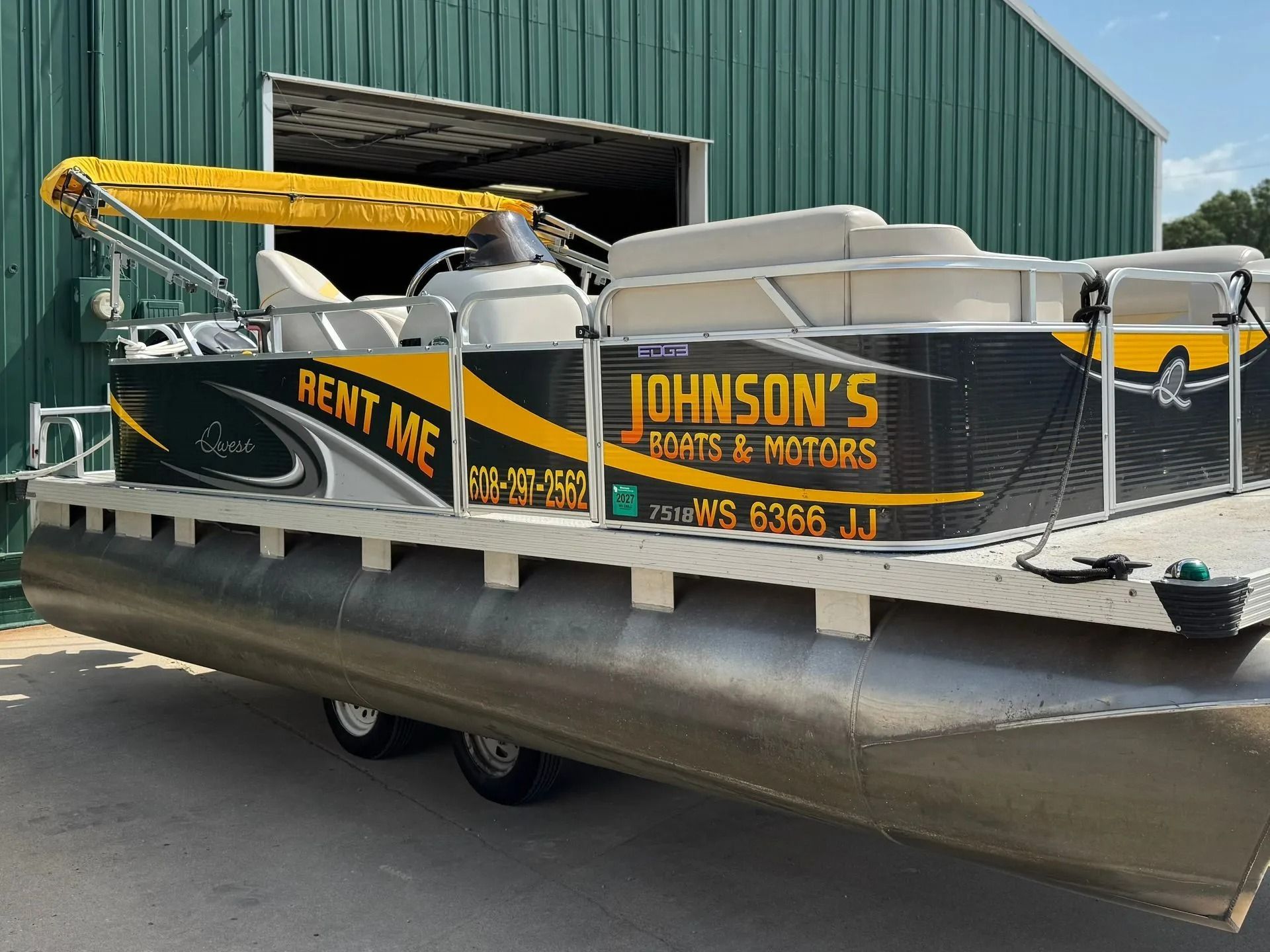 Yellow-and-black utility barge on a trailer outside a green warehouse, labeled “Johnson’s Docks & Motors”