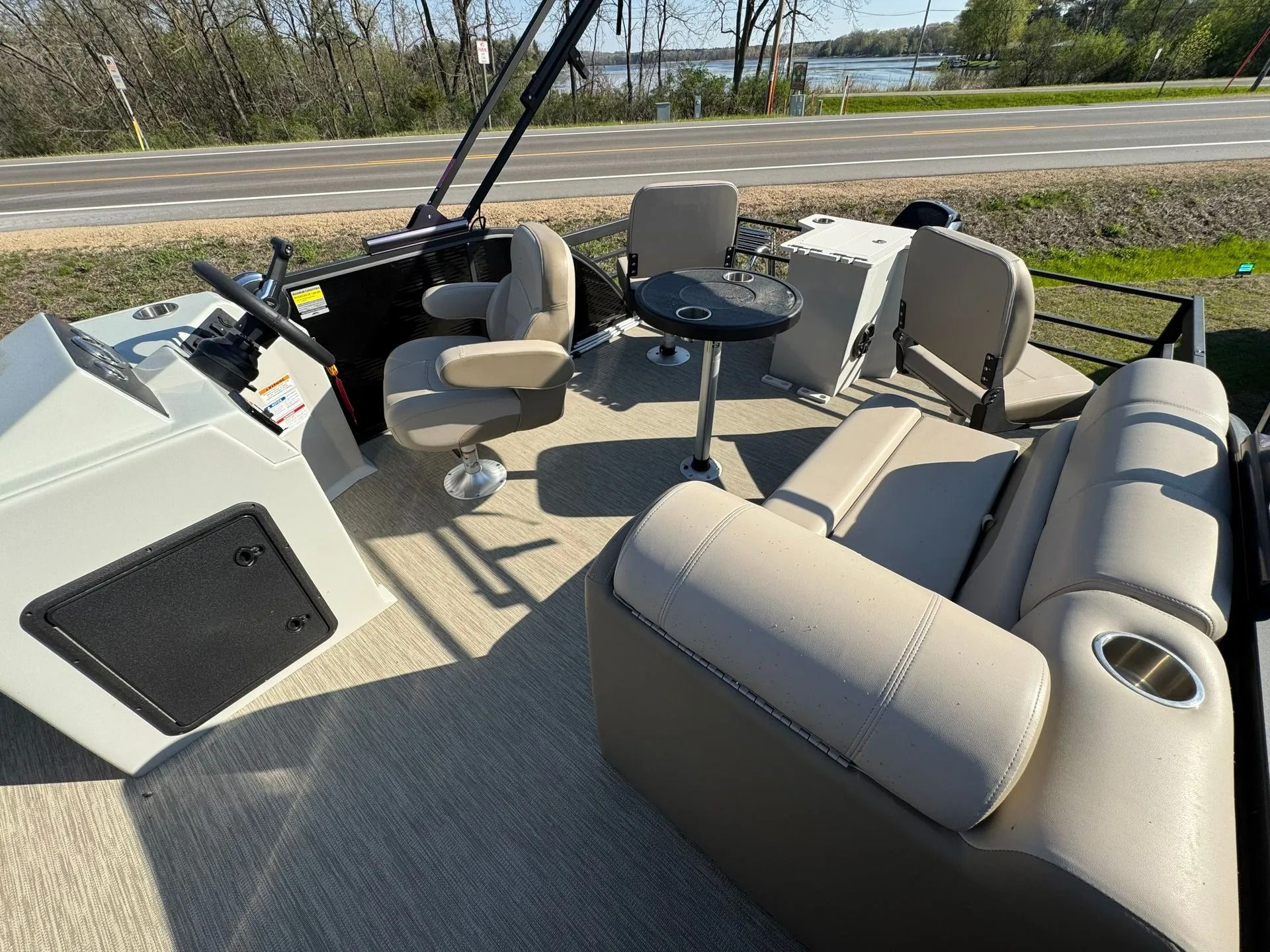 Boating cockpit with beige seats, steering wheel, windshield, and lake view beyond the bow.