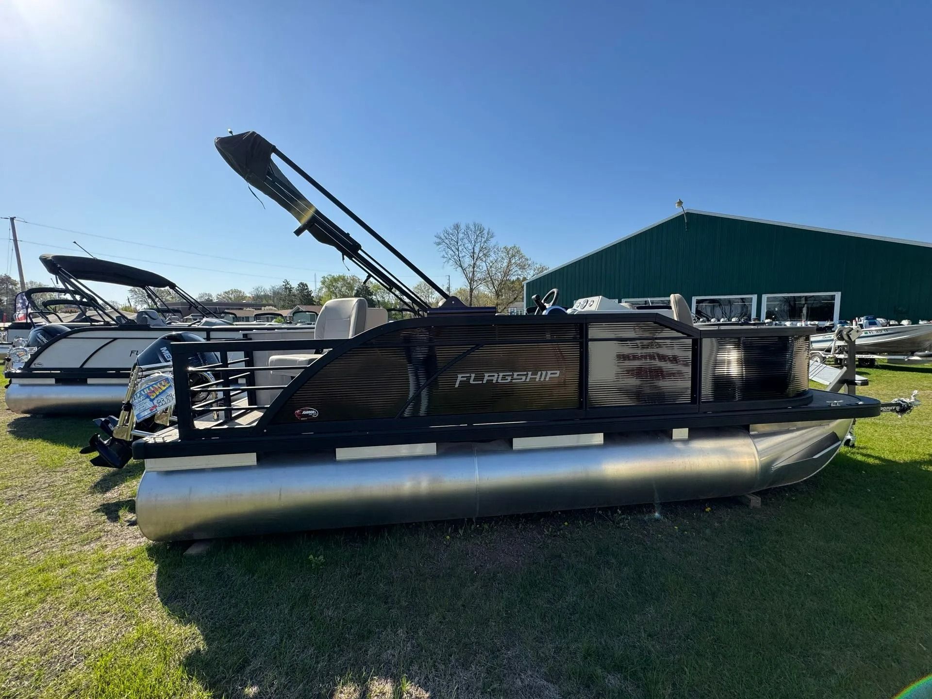 Pontoon boat on grass with raised canopy beside a marina building under a clear blue sky
