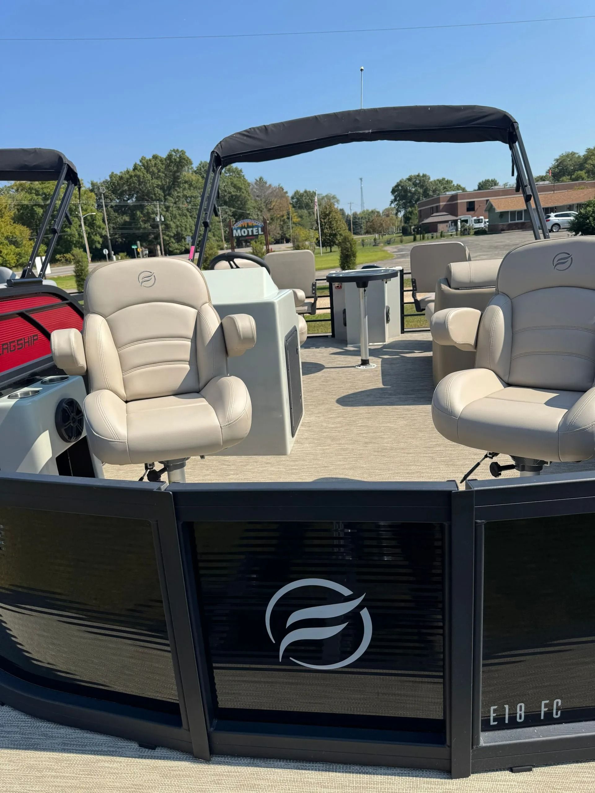 Pontoon boat with beige seating and black canopy on a sunny dockside waterway.