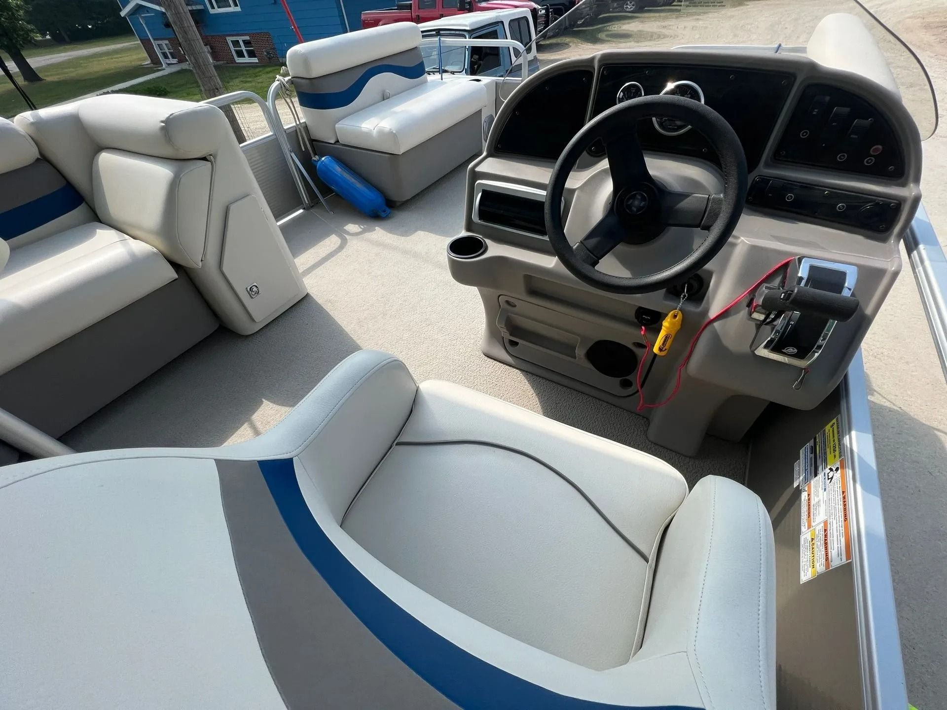Boat cockpit with white seats, black steering wheel, and blue accents on a sunny deck