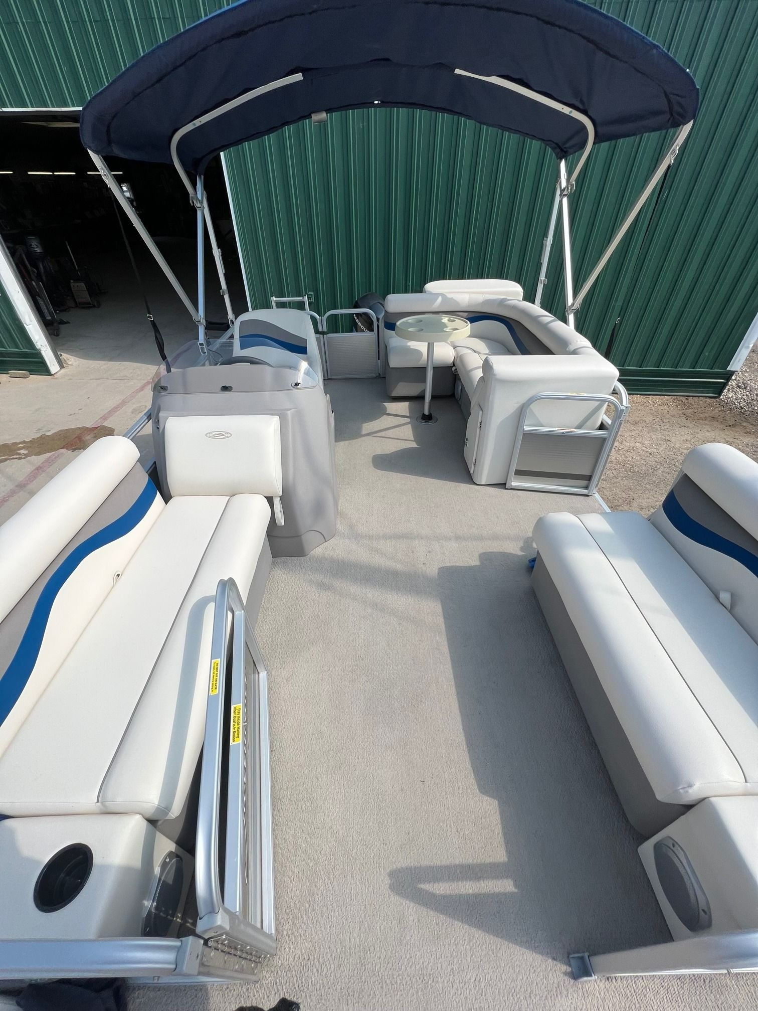 Pontoon boat seating area with white cushioned benches and a navy canopy on a dockside deck.