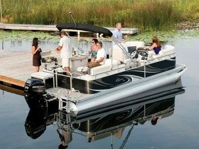 People relaxing on a pontoon boat docked on calm water near reeds
