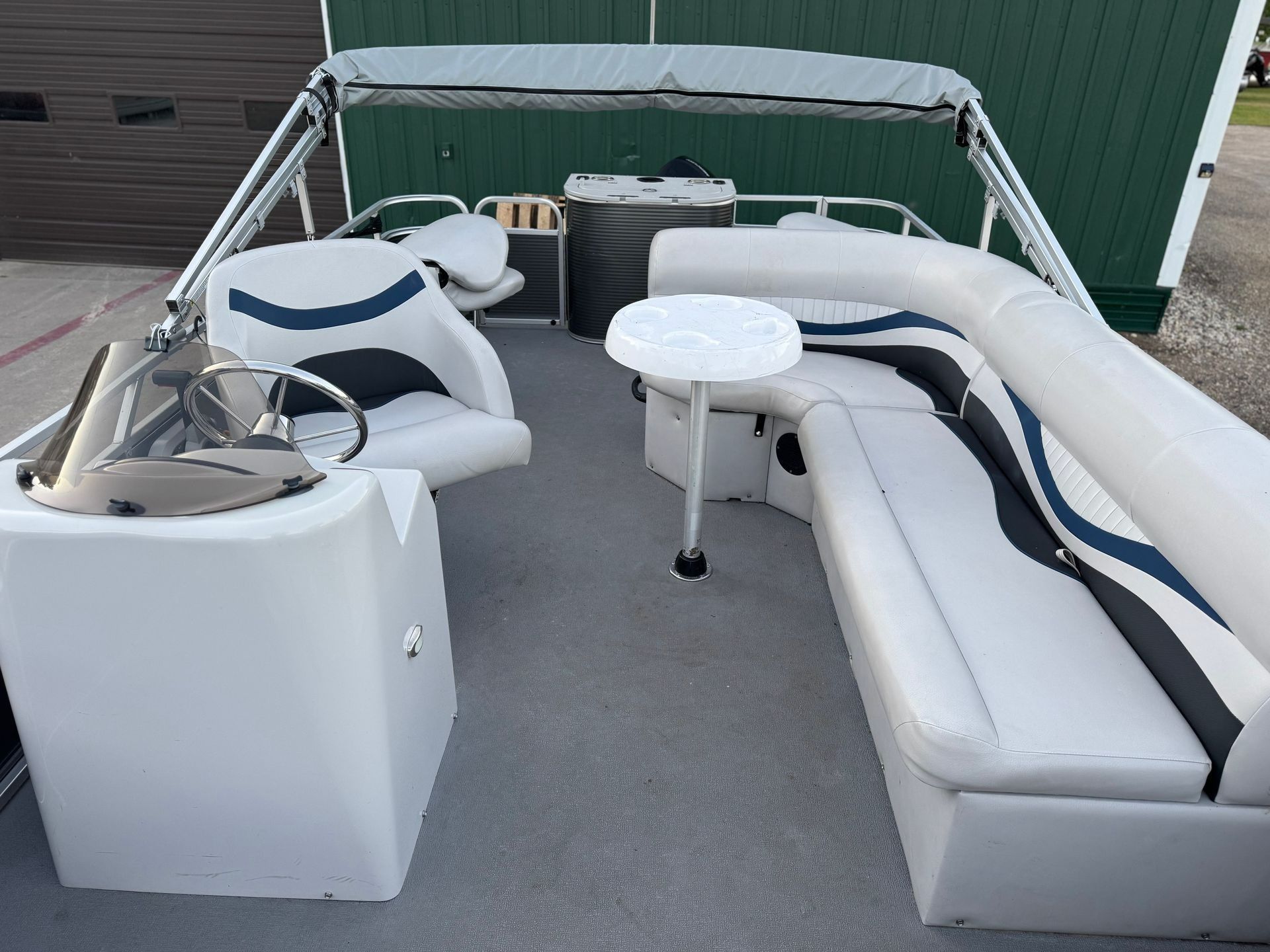 White patio boat seating with a table, shown outdoors beside a green building.