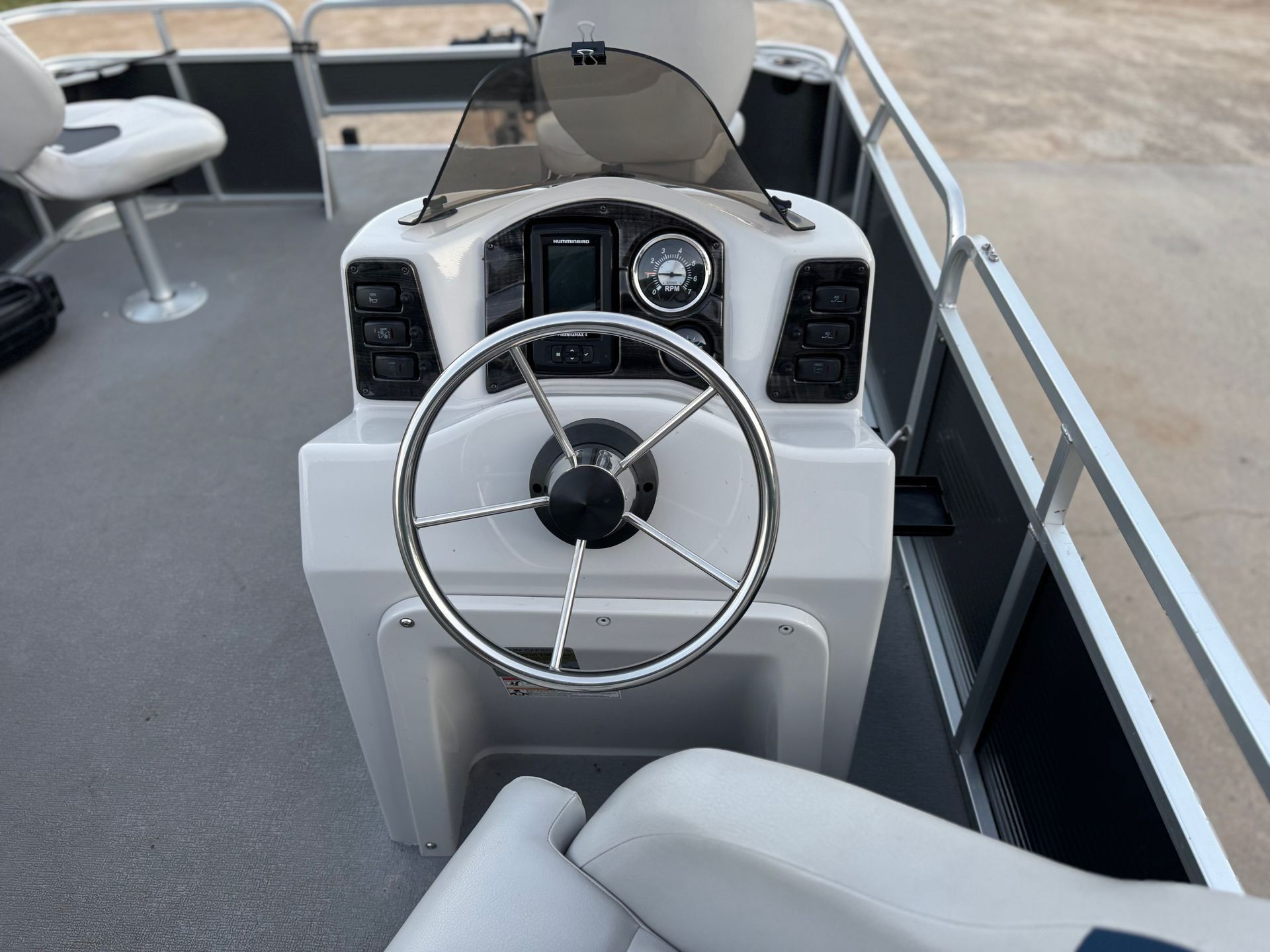 Boat helm with steering wheel, controls, and gray seating on a pontoon deck.