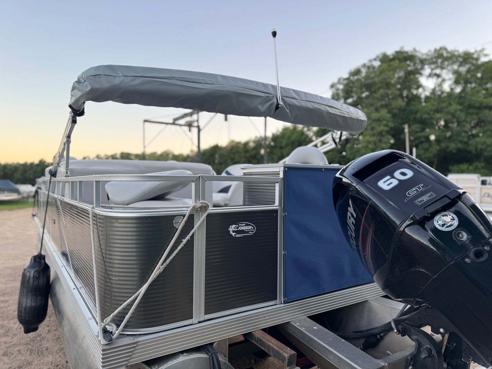 Pontoon boat at dock with gray canopy, blue cover, and a 60-hp outboard motor