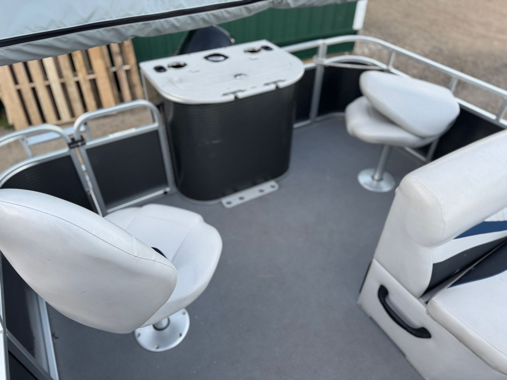 Small white boat cabin with two swivel seats, a table, and a green railing on the deck