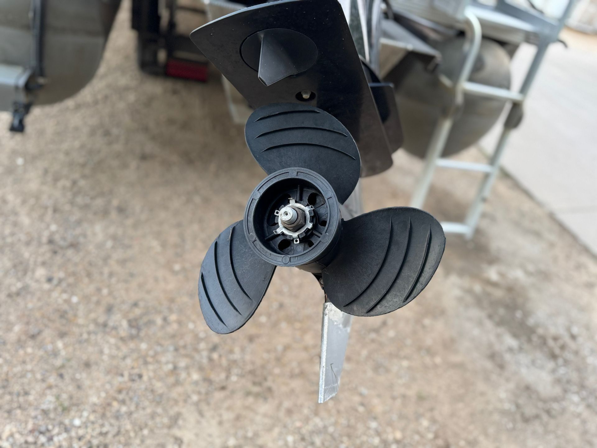 Close-up of a boat propeller with damaged blades on a gravel surface