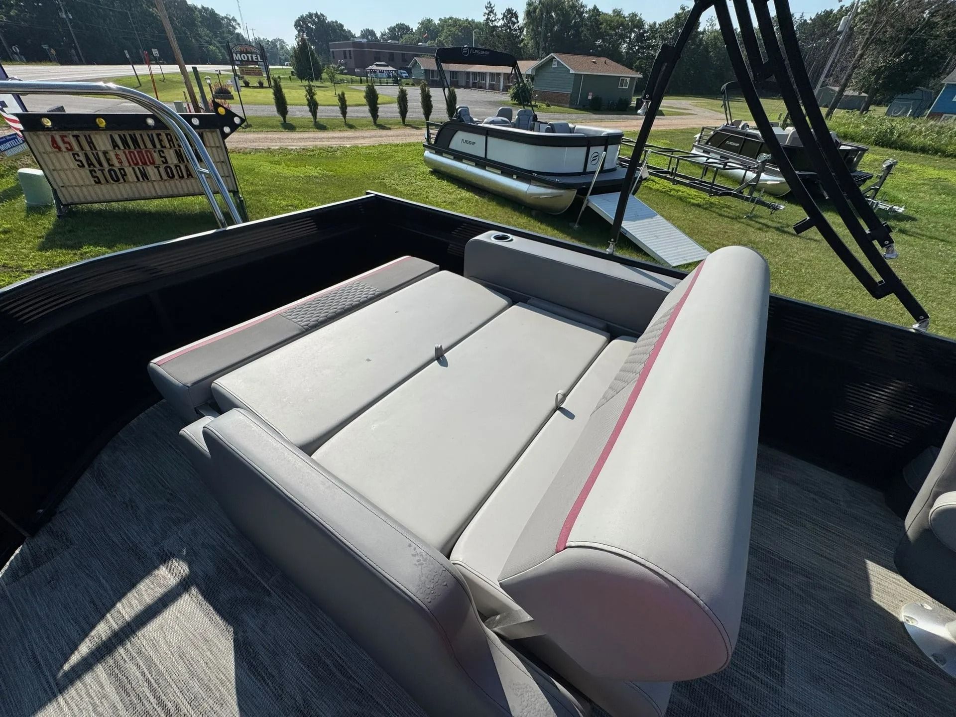 Gray outdoor bench seat with rolled armrests in a black trailer, parked near a pond and grassy field.