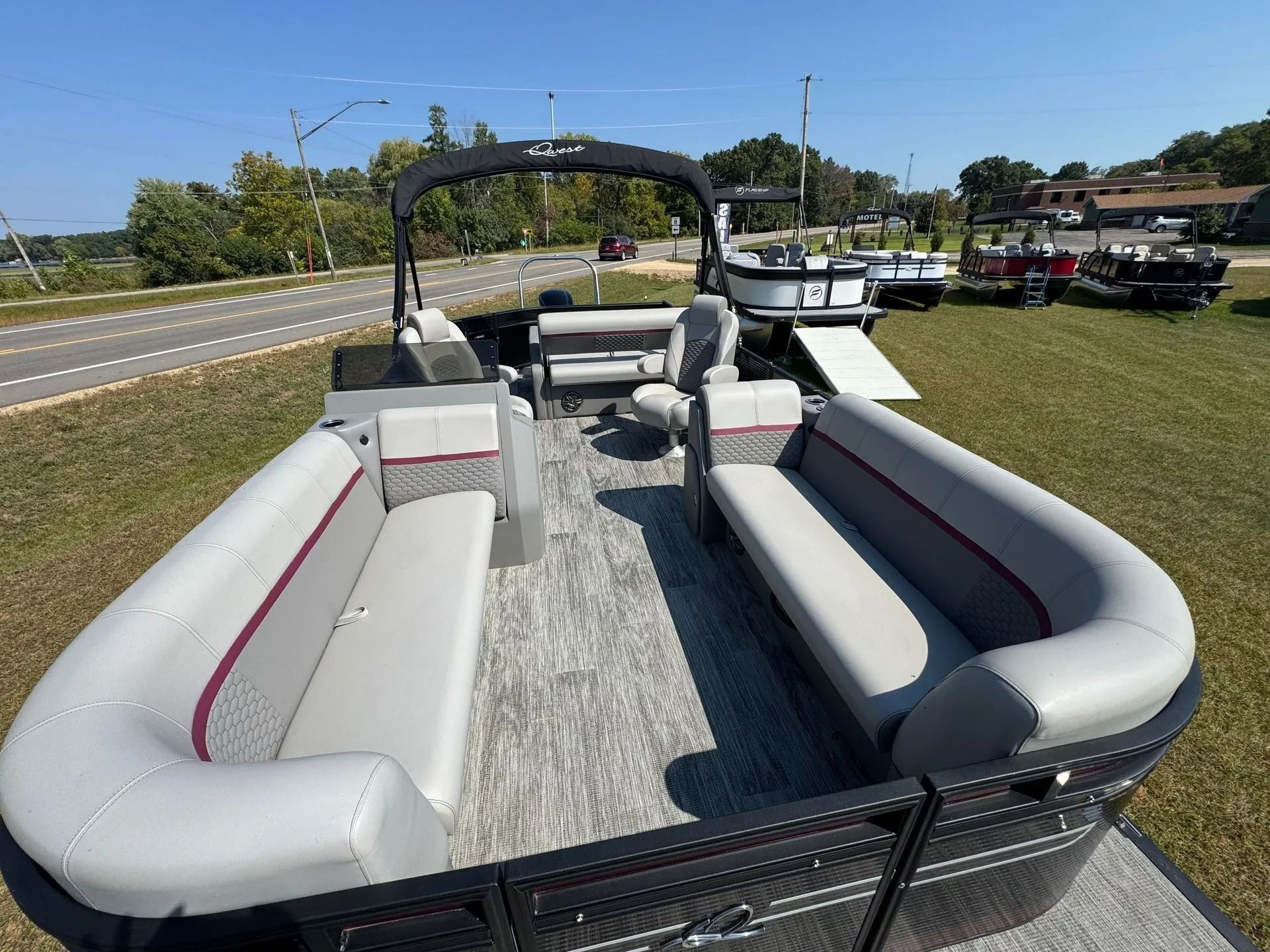 Pontoon boat with gray seats and black canopy parked on grass beside a road