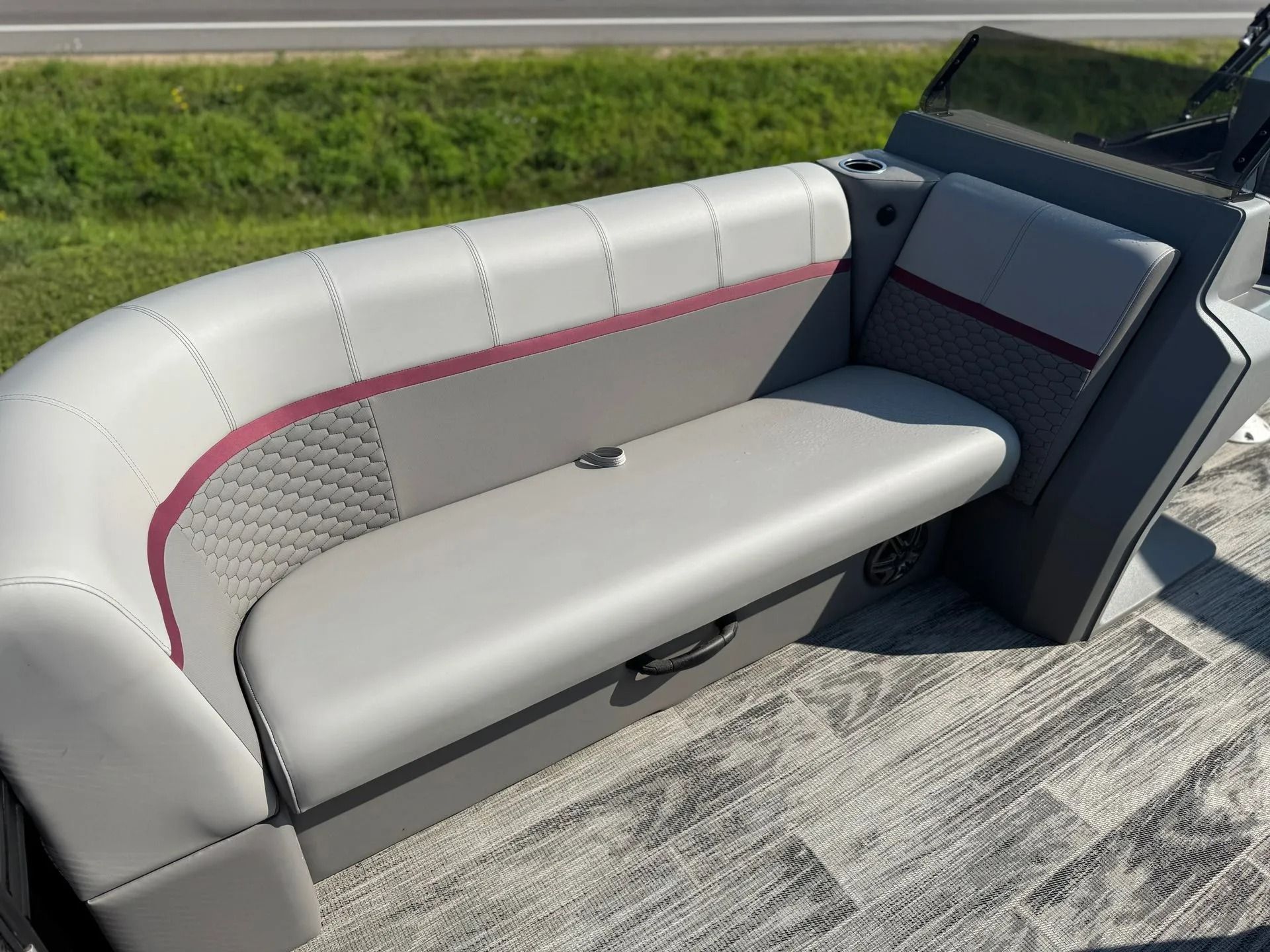 Gray and pink upholstered boat bench seat on a carpeted deck beside grassy shoreline