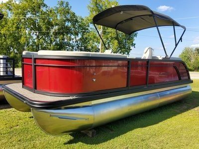 Red pontoon boat on grass with a black canopy, shiny aluminum hull, and trees in the background
