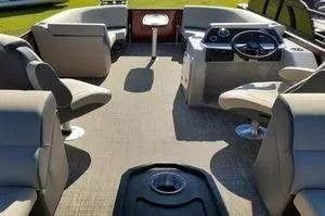 Pontoon boat interior with gray seats, helm console, and tan carpet on a lake.