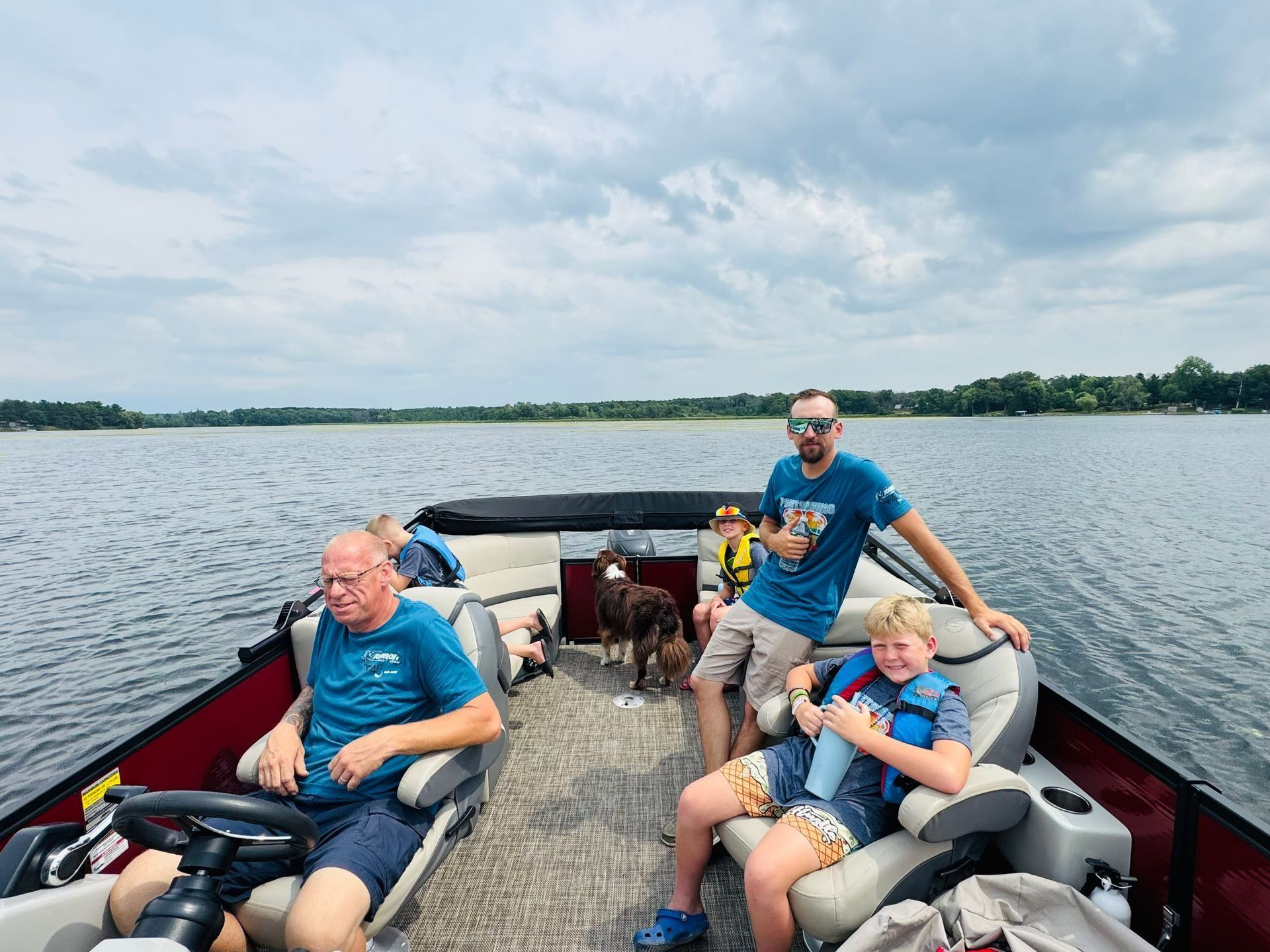 Four people relaxing on a pontoon boat on a lake under cloudy skies