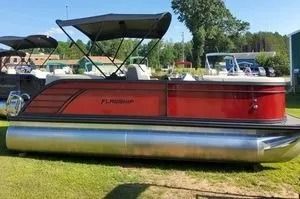 Red pontoon boat with black canopy on grass in a sunny outdoor setting