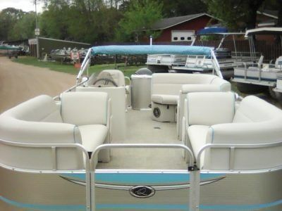 White pontoon boat with cream seating parked by a dock on a calm lakeside.