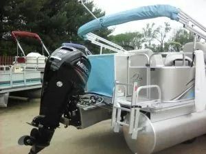 Pontoon boat with a black outboard motor and blue canopy docked on calm water.