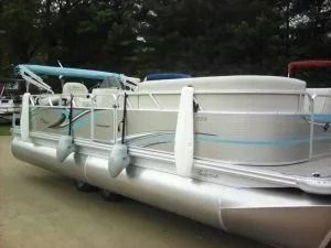 Pontoon boat with light blue trim docked on a muddy shore, with railings and white seats visible